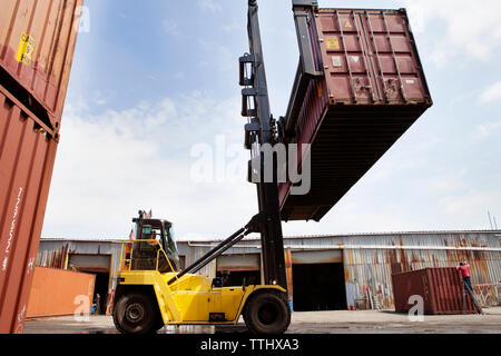 Uomo in sollevamento carrello contenitore di carico al dock commerciale contro sky Foto Stock