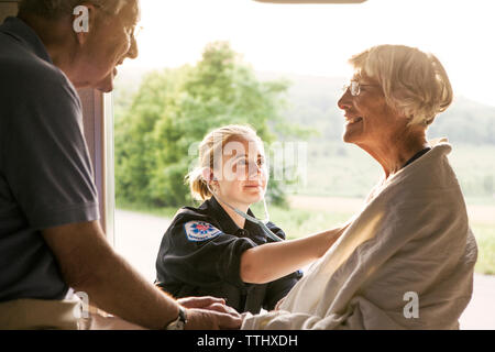 Felice paramedico esame paziente con uno stetoscopio da marito in ambulanza Foto Stock