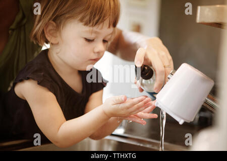 Immagine ritagliata della madre che assiste la figlia di lavaggio delle mani a casa Foto Stock