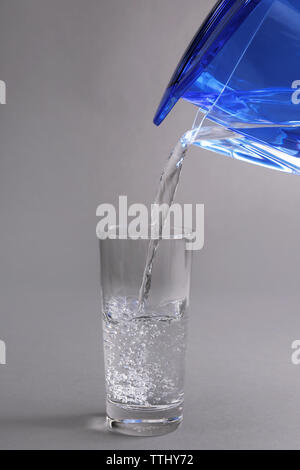 Caraffa filtro versando acqua in vetro su uno sfondo grigio, close-up Foto Stock