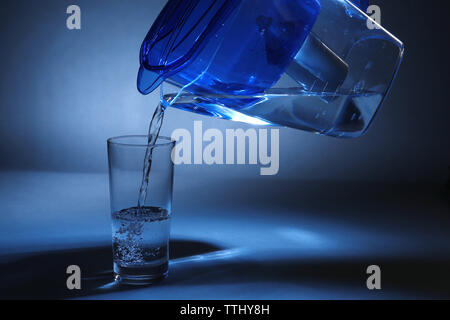 Caraffa filtro versando acqua in vetro, su sfondo scuro Foto Stock