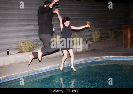 Coppia con tenendo le mani del salto in piscina Foto Stock