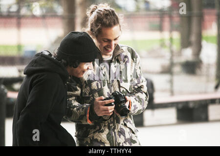 Uomo che mostra fotografie ad un amico durante il riposo a skate park Foto Stock