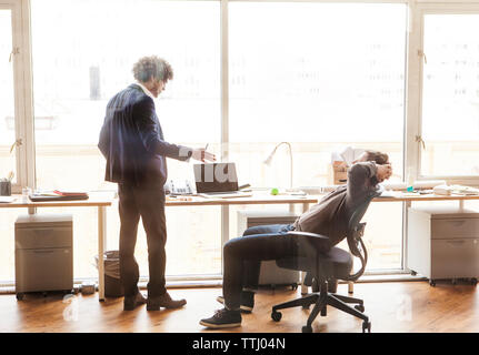 uomo d'affari che spiega mentre un collega si rilassa sulla sedia in ufficio Foto Stock