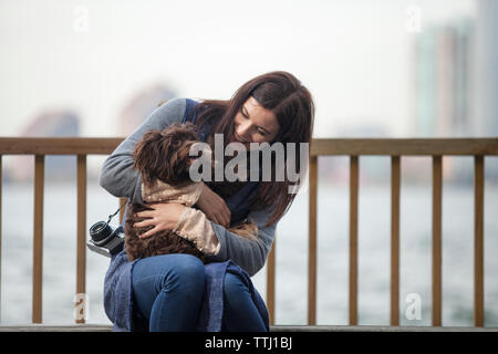 Donna che guarda cane mentre è seduto sulla panchina contro il fiume Hudson Foto Stock