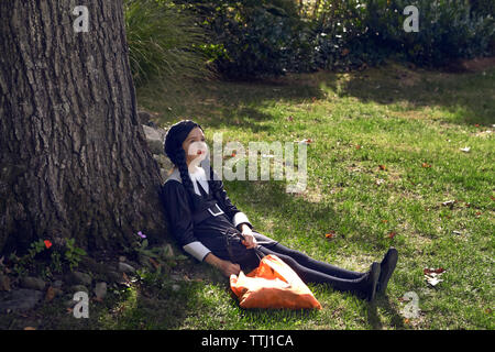 Ragazza in costume seduta dal tronco di albero in Prato Foto Stock