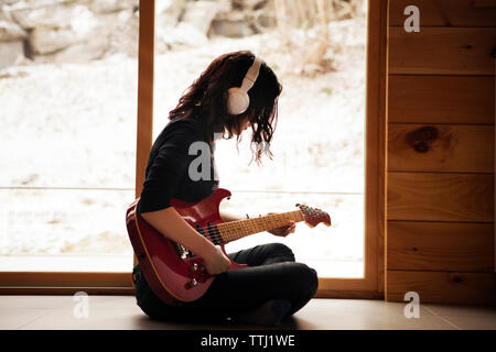 Vista laterale della ragazza adolescente a suonare la chitarra mentre è seduto sul pavimento a casa Foto Stock