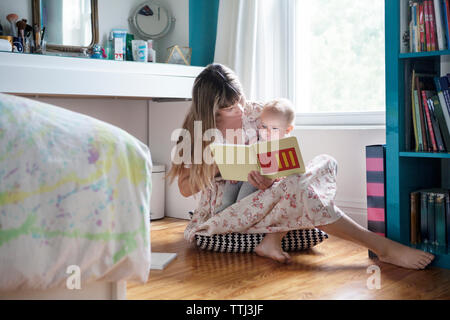 Madre libro di lettura con il bambino seduto sul pavimento a casa Foto Stock