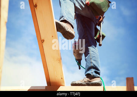Sezione bassa del lavoratore con trapano in piedi sul telaio di legno contro sky Foto Stock