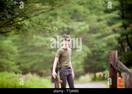 Ragazzo adolescente holding skateboard mentre in piedi contro alberi Foto Stock