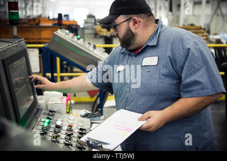 Il sovrappeso lavoratore manuale funzionamento di macchinari al pannello di controllo nella industria del metallo Foto Stock