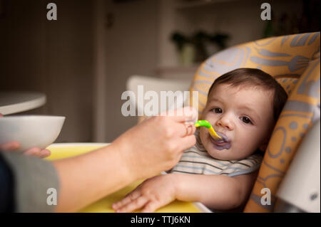 Immagine ritagliata della madre di alimentazione manuale baby boy a casa Foto Stock