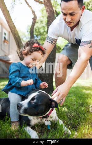 Padre assistere ragazza seduta sul cane nel cortile posteriore Foto Stock