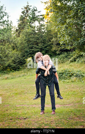 Ritratto di giovane piggybacking mentre si sta in piedi sul campo Foto Stock