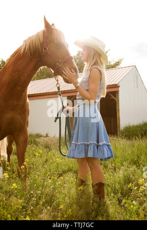 Vista laterale del cowgirl stroking cavallo mentre si sta in piedi sul campo Foto Stock