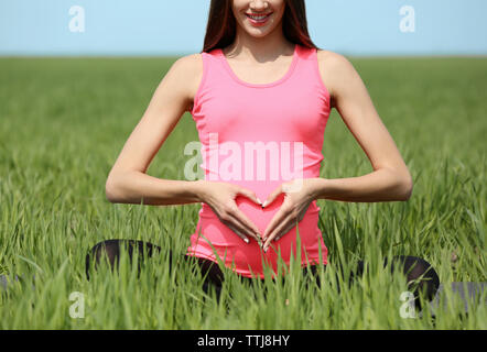 Donna incinta messa a forma di cuore con le mani nel campo Foto Stock