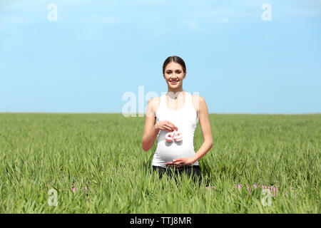 Donna incinta holding baby's bootees nel campo Foto Stock