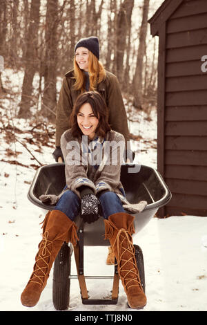 Donna spingendo amico seduto in carriola sul campo di neve Foto Stock