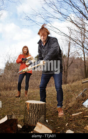 Donna che guarda al ragazzo il taglio di log Foto Stock