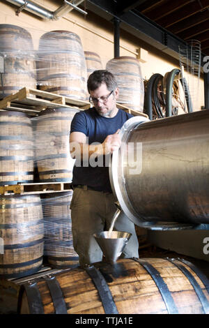 L'uomo versando il vino in contenitore in fabbrica Foto Stock