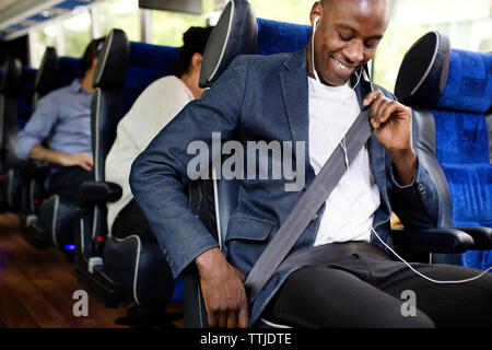 Uomo felice regolazione della cintura di sicurezza durante la seduta in autobus Foto Stock