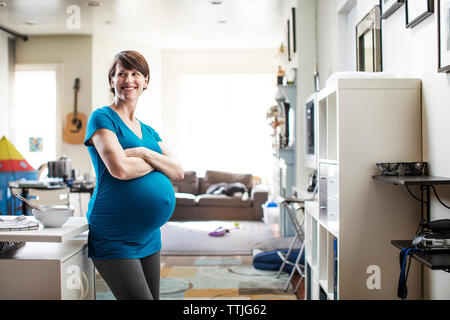 Donna incinta con le braccia incrociate che guarda lontano rimanendo a casa Foto Stock