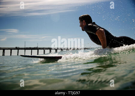 Vista laterale dell'uomo surf in mare contro sky Foto Stock