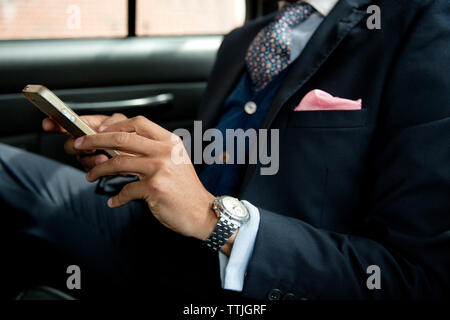 Immagine ritagliata di imprenditore utilizzando il telefono cellulare mentre è seduto in auto Foto Stock