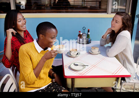 Happy amici con cappuccino seduti al cafè sul marciapiede Foto Stock