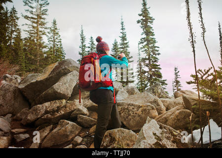 Vista laterale della donna fotografare mentre in piedi da rocce Foto Stock