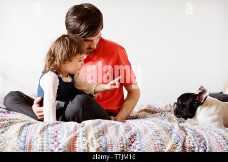 Ragazza puntando al cane mentre è seduto con il padre sul letto Foto Stock