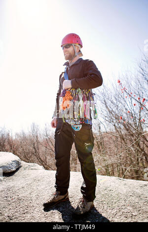 Uomo con attrezzatura per le escursioni alla ricerca di distanza mentre in piedi sulle rocce contro il cielo chiaro Foto Stock