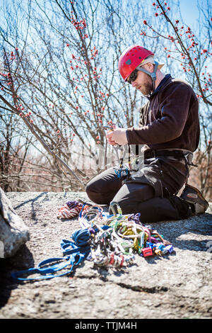 Vista laterale dell'uomo preparando per rappelling mentre inginocchiarsi sulle rocce Foto Stock
