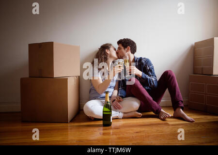 Coppia con wineglasses kissing mentre è seduto sul pavimento a casa Foto Stock