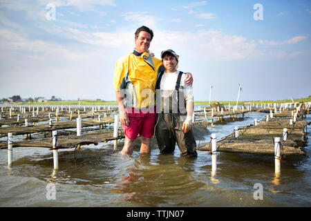 Ritratto di uomini con le braccia intorno a piedi in oyster farm Foto Stock
