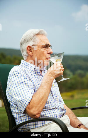 Senior uomo bevendo Martini mentre è seduto su una sedia in Prato Foto Stock