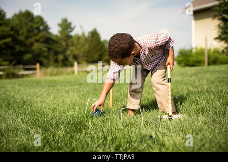 Ragazzo giocando croquet mentre si sta in piedi sul campo erboso in cortile Foto Stock