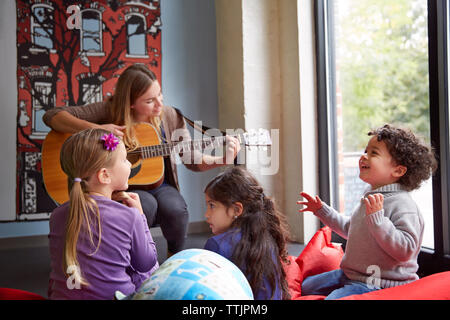 Insegnante a suonare la chitarra mentre godendo i bambini in età prescolare Foto Stock