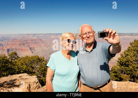 Giovane tenendo selfie mentre si sta in piedi sul monte contro il cielo blu chiaro Foto Stock