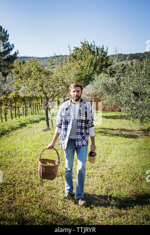 Ritratto di uomo con cestello e bottiglia di vino mentre si sta in piedi sul campo in vigna Foto Stock