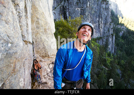 Uomo felice cercando mentre in piedi dalla formazione di roccia contro la montagna Foto Stock