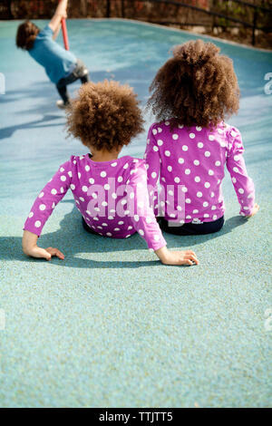 Vista posteriore dei bambini seduti nel parco giochi Foto Stock
