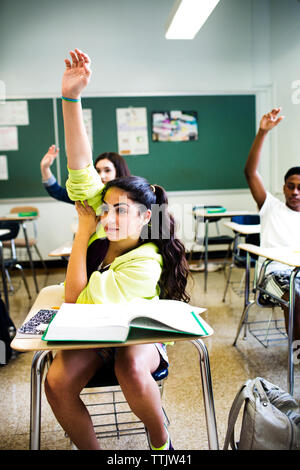 Gli studenti alzando le mani durante la lezione in aula Foto Stock