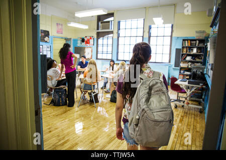 Vista posteriore di una ragazza in piedi in aula con docente e compagni di classe in background Foto Stock