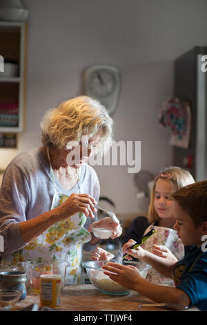 Donna aggiunta di zuccheri in pasta mentre rendendo i cookie con i bambini in cucina Foto Stock