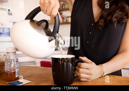 Sezione mediana della donna versando acqua nella tazza in cucina Foto Stock