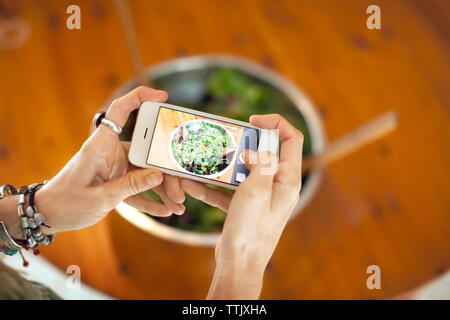 Immagine ritagliata della donna fotografare insalata in ciotola Foto Stock