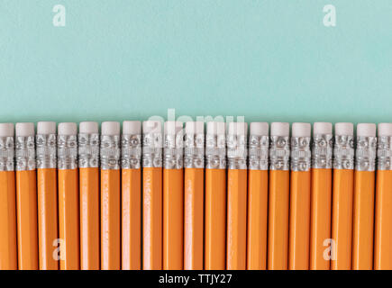 Confine di matite di colore arancione con gomme, su un verde blu sfondo con spazio di copia Foto Stock