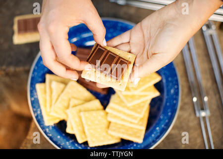 Immagine ritagliata delle mani preparazione smores durante il summer camp Foto Stock