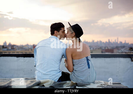 Vista posteriore del giovane kissing seduti sulla terrazza edificio durante il tramonto Foto Stock